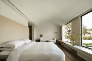 A minimalist bedroom with a white bed and walls, showcasing modern design principles and simplicity.