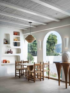 A minimalist dining room with concrete walls, wood furniture, and a modern chandelier.