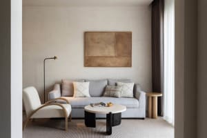 A modern minimalist living room with neutral tones, a grey sofa with patterned cushions, and a round coffee table with a lamp
