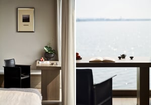 A modern residential space featuring a wooden table with fruit and books, overlooking a serene water vista.