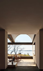 A modern lounge area featuring a wooden floor and furniture, with a large window overlooking a serene lake.