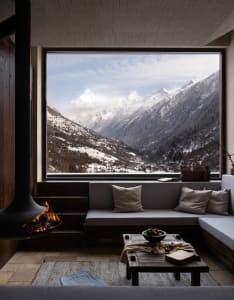 Modern minimalist living room featuring a gray sectional sofa with pillows and a coffee table with a bowl of fruit and books.