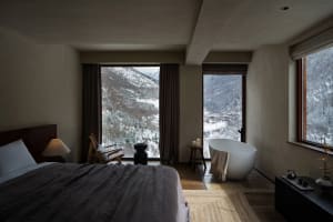 A modern bedroom featuring a carpeted floor, minimalistic furniture, and a view of snowy mountains through large windows.