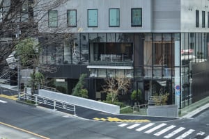 Modern city coffee shop facade with glass front and greenery.