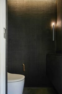 A modern minimalist bathroom with dark, textured walls coated in natural fibers.