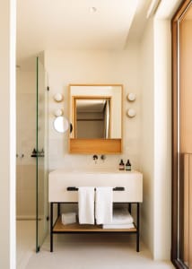 Modern minimalist bathroom with concrete sink and flooring, white towels, and wooden accents.