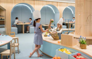 Children playing in a modern, brightly lit playroom with wooden furniture and natural materials.