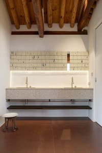 Modern bathroom featuring a granite countertop with two sinks, a wooden ceiling with exposed beams, and under-cabinet lightin
