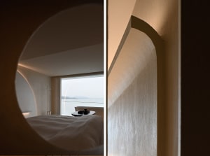 A modern minimalist bedroom featuring concrete walls and a view of the ocean through a large window.