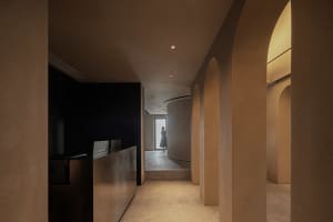 A modern architectural corridor with arched openings and concrete walls, featuring a person standing in the distance.