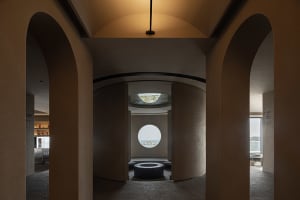 A minimalist restaurant interior with a concrete floor and circular windows.