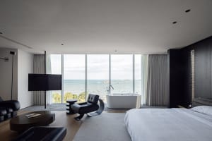 A modern bedroom featuring concrete walls and a large window with a view of the ocean.