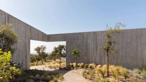 A minimalist residential exterior with a concrete wall and natural landscape.