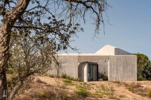 A modern house made of concrete with a minimalist design, surrounded by trees and vegetation.