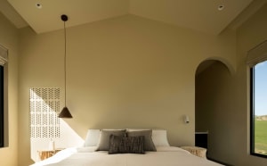 Modern minimalist bedroom featuring a bed with a white duvet and neutral-colored accent pillows, set against a beige wall and