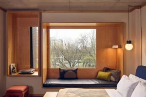 A minimalist bedroom featuring a wooden bench along the window with cushions and a record player.