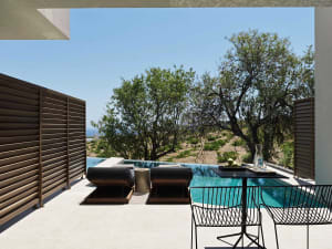 Modern, minimalist outdoor residential pool deck with concrete patio, lounge chairs, table, and infinity pool.