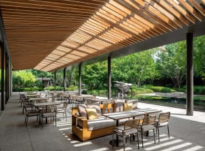 A modern outdoor seating area with wooden pergola, concrete floor, and steel columns.