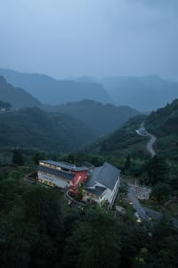 Modern residential architecture featuring concrete and glass materials, set against a backdrop of lush green hills and mounta