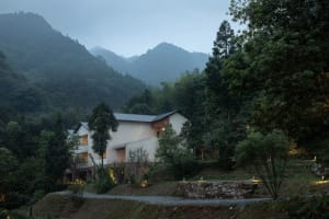 A modern residential exterior with concrete walls and a sloped roof in a forested area.