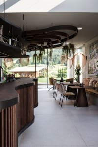 A modern restaurant interior featuring wooden tables, metal chairs, and hanging plants.