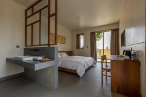 Minimalist hotel bedroom with concrete tiles, wooden furniture, and a large window.