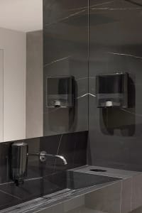 A modern bathroom featuring black marble walls and a white sink with a silver faucet.