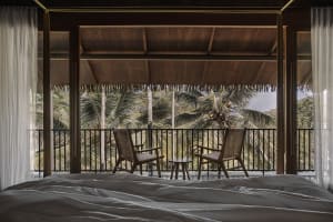 An inviting balcony featuring a wooden table and two woven chairs overlooking tropical foliage.