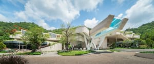 A modern concrete cliff house with a glass roof and outdoor greenery.