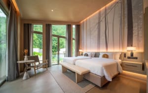 Modern minimalist bedroom featuring glass windows, wood flooring, and cotton bedding.
