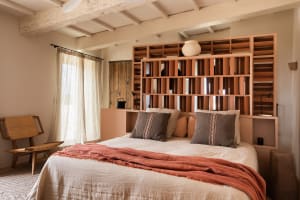 A cozy bedroom with a wooden bookshelf as the focal point, featuring comfortable bedding and a rustic chair.