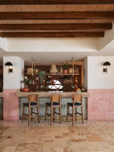 A restaurant bar featuring wooden stools, concrete flooring, and a glass partition.
