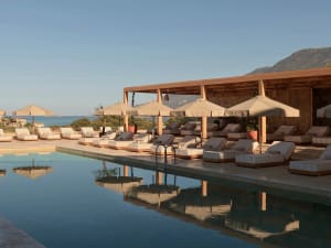 Swimming pool area with sun loungers, umbrellas, and a wooden canopy overlooking the sea.