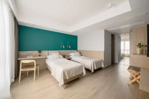 A modern minimalist bedroom with twin beds, wooden headboards, and a green accent wall.