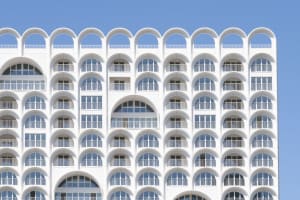 A modern building with a white, concrete exterior featuring repetitive arches and balconies.
