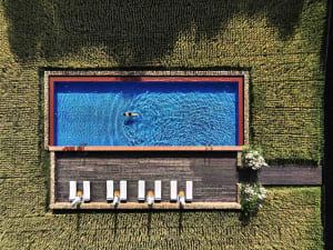 Aerial view of a rectangular swimming pool surrounded by a wooden deck, located within a field of tall grass.