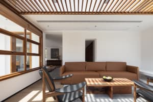 A minimalist living room with a brown leather sofa, black armchairs, and a wooden coffee table.