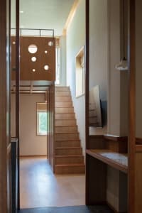 A modern interior space featuring wooden stairs with circular cutouts, natural light, and a wooden desk.