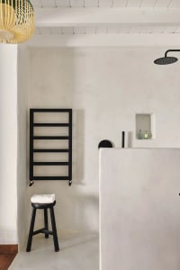 A minimalist bathroom with a concrete floor, wooden stool, and black towel rack.