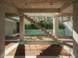 A minimalist staircase with concrete steps and steel railings adjacent to a swimming pool, set against a backdrop of green fo