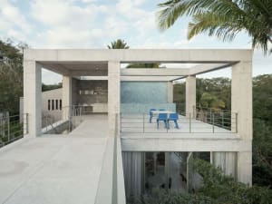 A modern rooftop deck made of concrete with a concrete wall and a blue table and chairs.