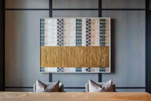 A modern dining room featuring a wall adorned with various patterned tiles in shades of beige and gold, with a wooden table a