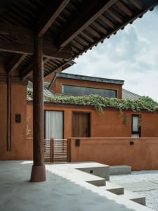 Modern residential exterior with terracotta clay walls and a metal roof structure.
