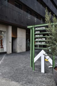 Black building facade with concrete columns and a green metal sign featuring text in white.