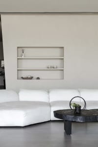 A minimalist living room with a large white sofa and a black coffee table on a concrete floor.