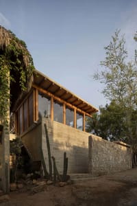 Modern residential house with concrete walls, stone foundation, and thatched roof.