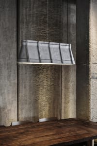 A metal cylindrical pendant light fixture hanging from a concrete wall.