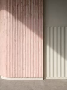 A modern interior design featuring a textured marble wall with vertical lines and shadows created by sunlight.