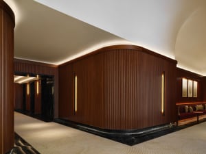 A modern lobby featuring dark wooden walls with vertical ribbing and recessed lighting. The room has a sleek, contemporary de