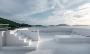 A minimalist concrete terrace overlooking the sea with a staircase and seating area.